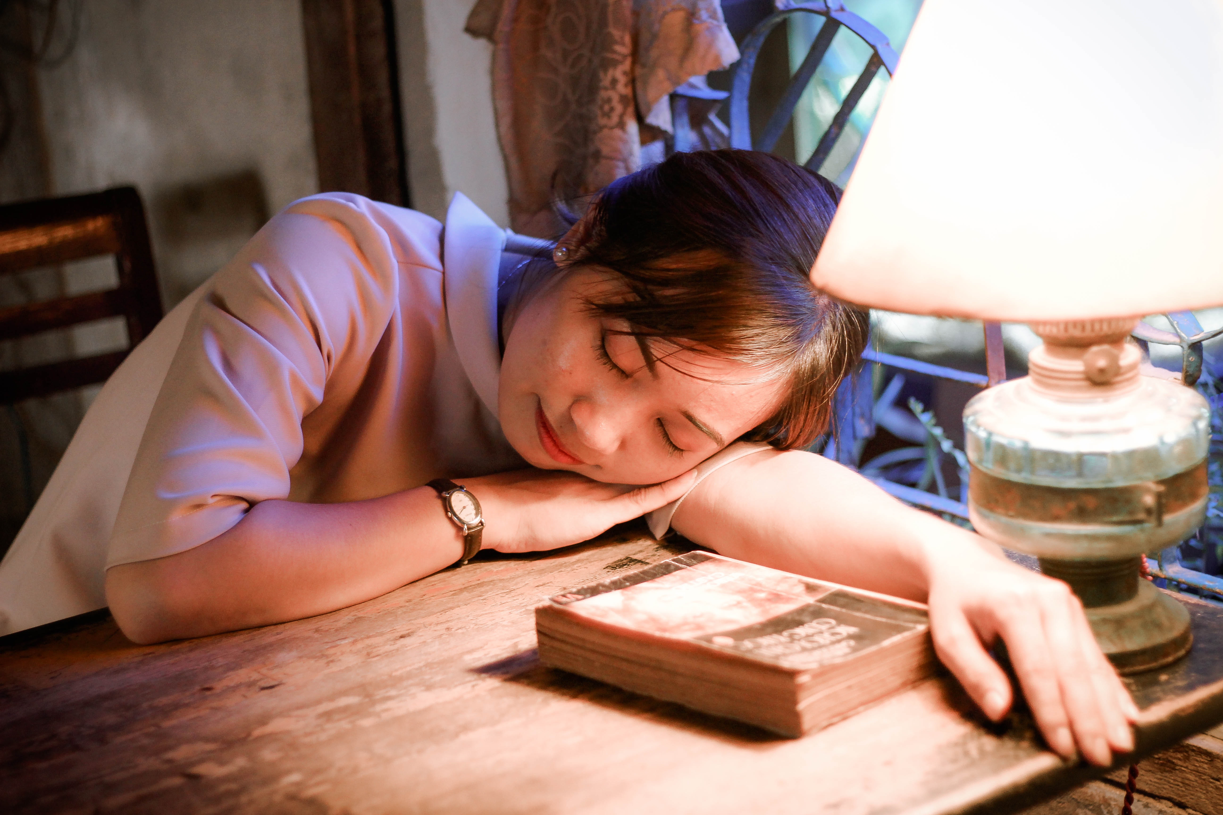 A young girl asleep with her head on a desk next to a book.