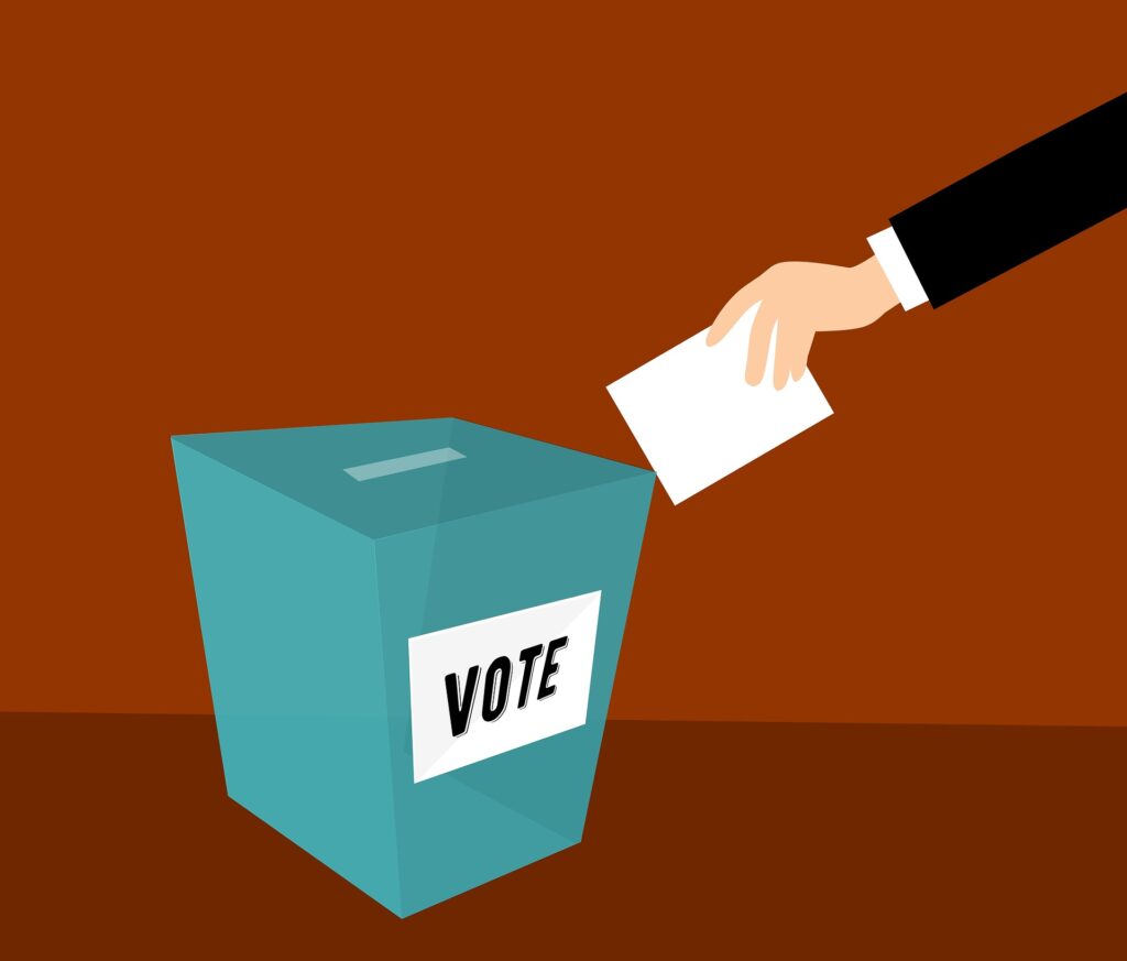 A man putting a ballot in a voting box. Rhode Island is bringing real voting machines into schools for some student elections as a learning opportunity.