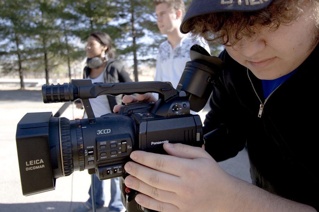 Close up of a student looking down at a video camera while filming.