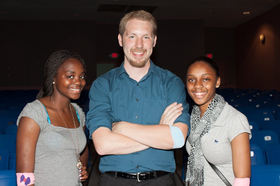 A man is standing in between two young women, and each of them has a bandage on their arm from donating at a blood drive.