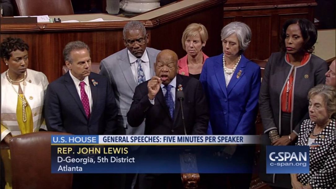 Rep. John Lewis giving a floor speech on the House floor with other Representatives standing behind him.