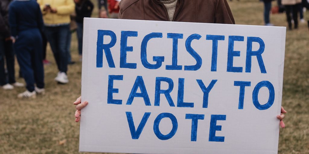 Man holding a sign saying, "Register Early to Vote"